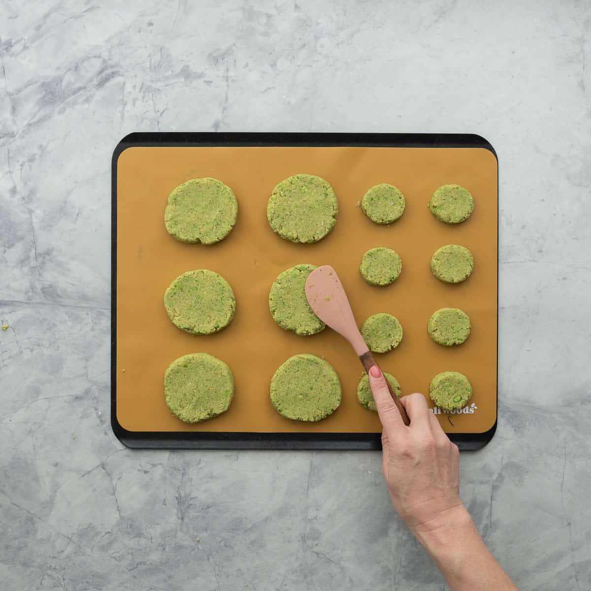 Patties on baking tray being flattered by spatula.