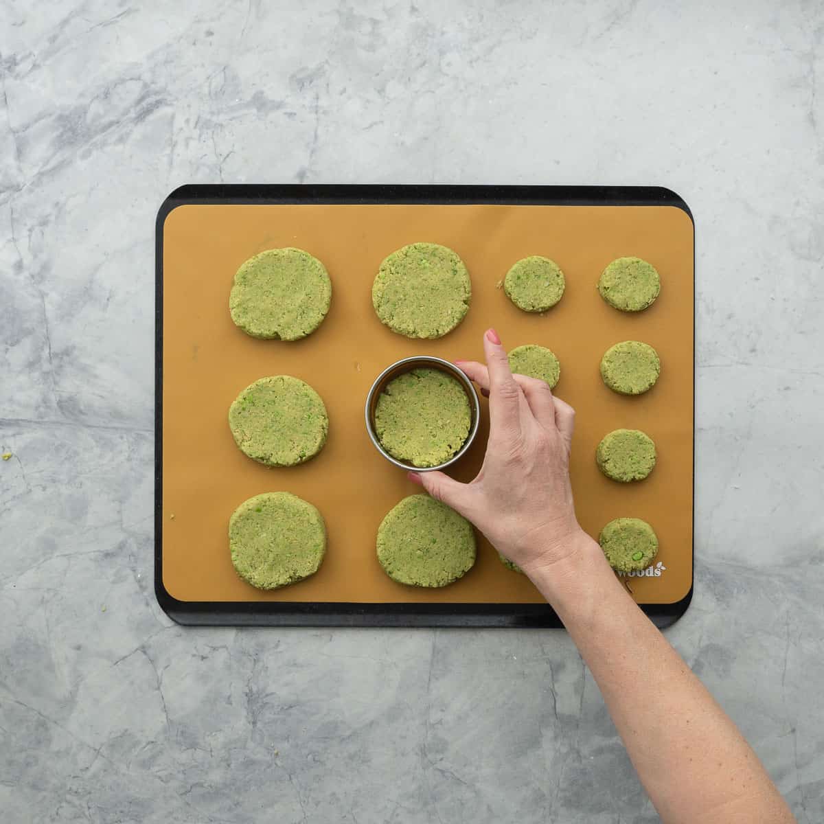 Hand holding a circle cookie cutter around a patty to form a perfect circle.