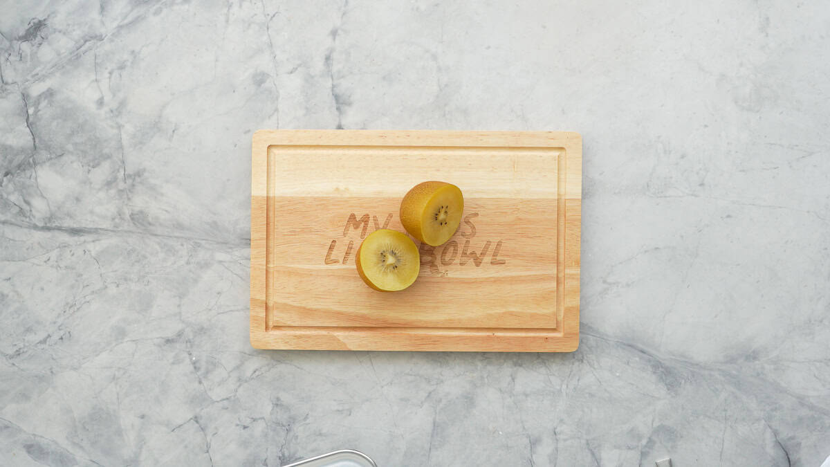 One gold kiwi cut in half on a wooden chopping board. 