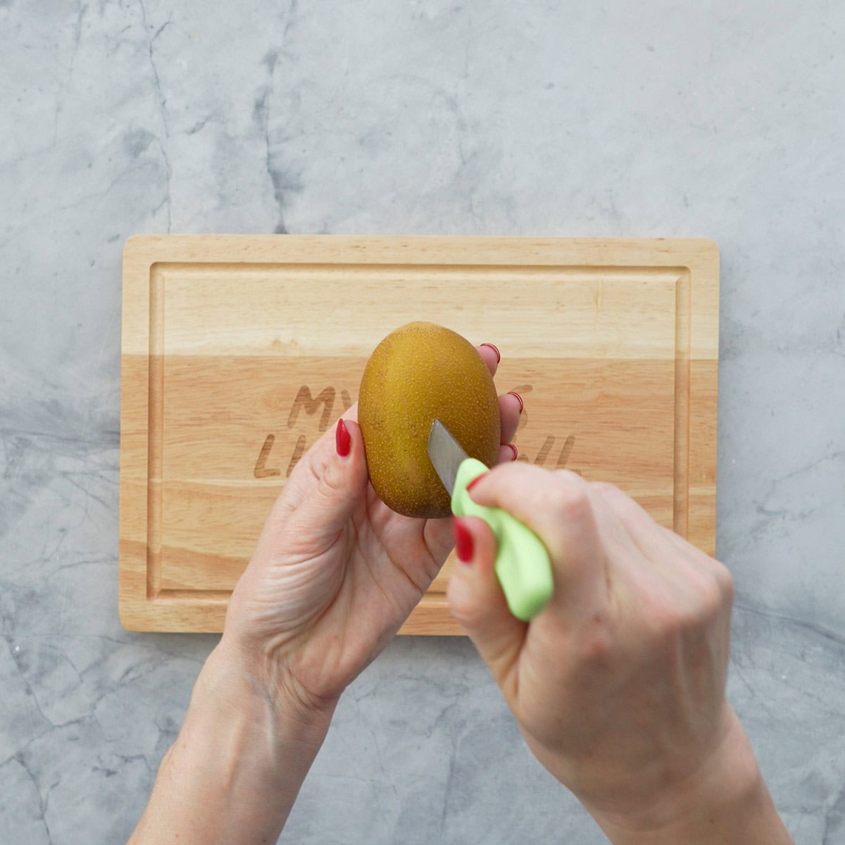 The tip of a small green handled knife being pushed into a gold kiwifruit. 