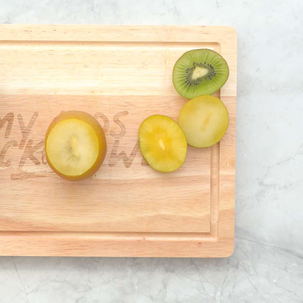 A gold kiwi that has both ends removed sitting upright on a wooden chopping board.