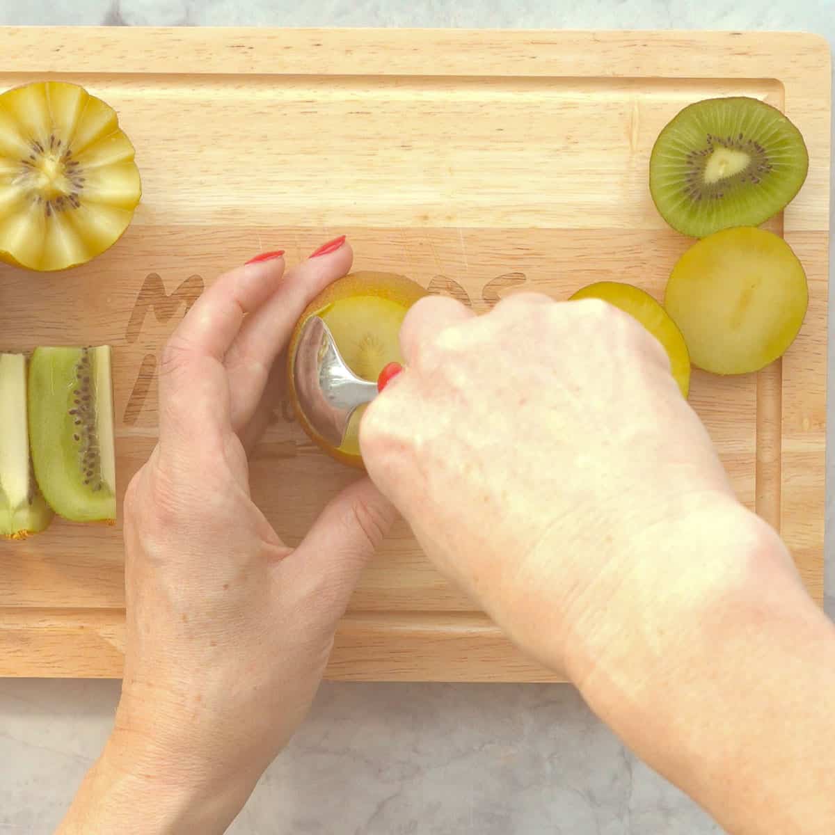 A dessert spoon being used to separate kiwi flesh from the skin. 