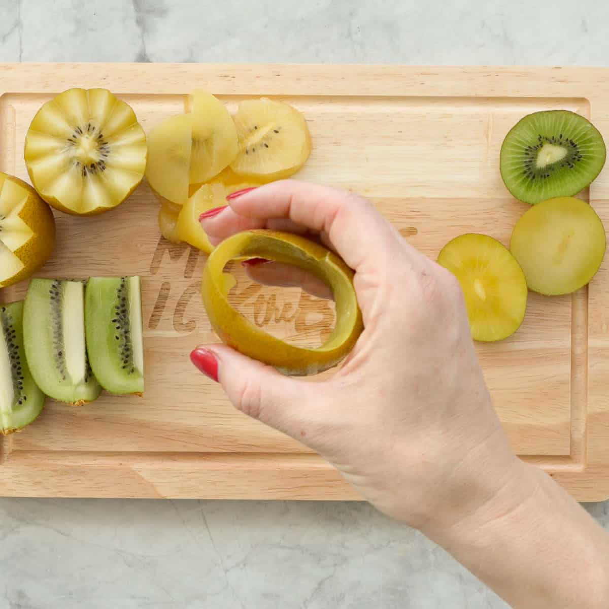 A hand holding a gold kiwifruit skin that has been removed in one piece. 