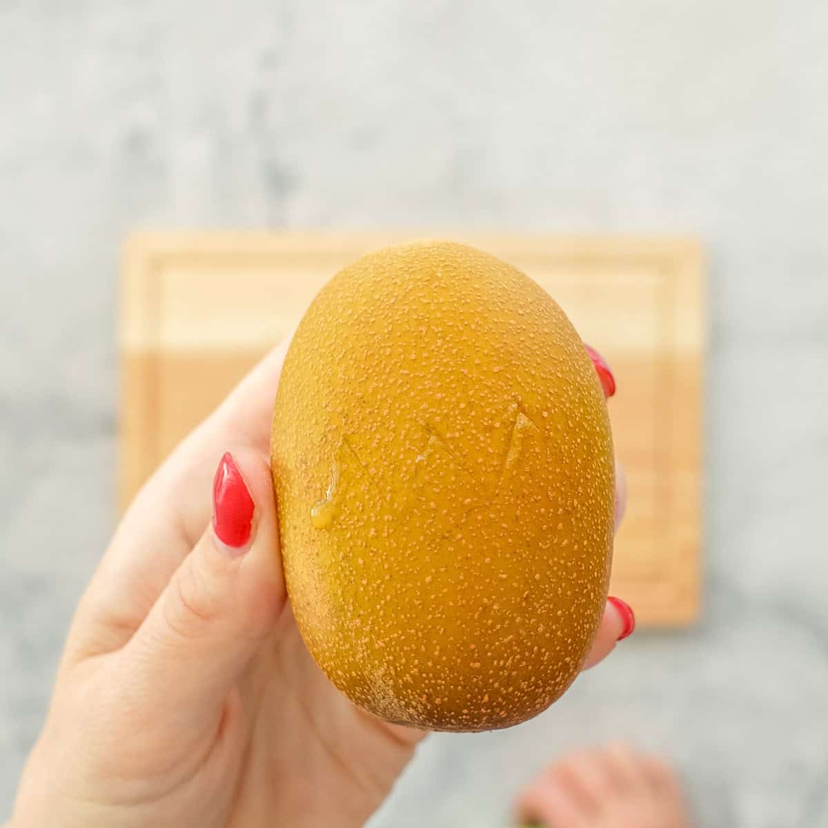 A hand holding up a kiwi with horizontal zigzag cut through the centre around the whole fruit.