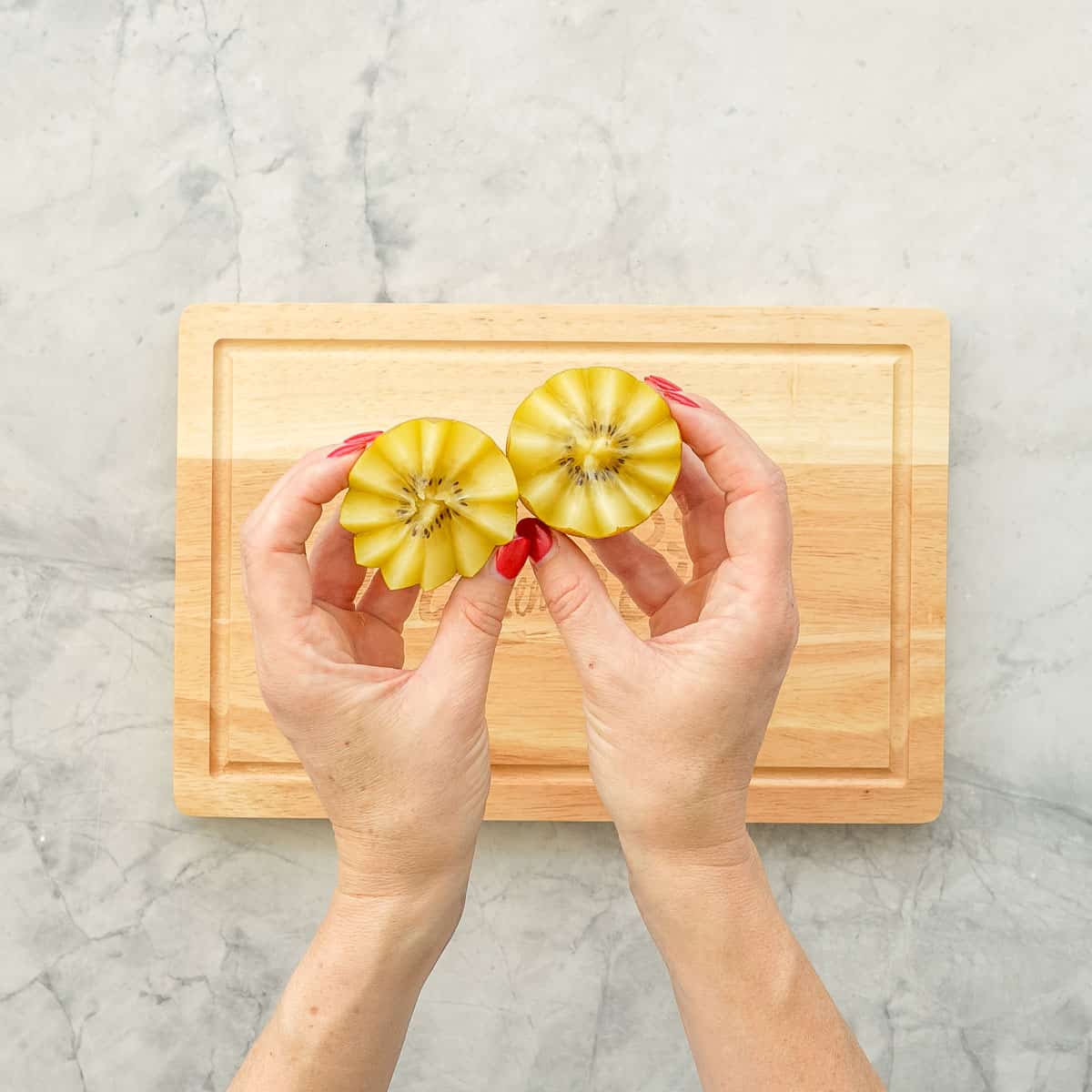 Hands holding the cut up kiwi with the zigzag pattern showing.