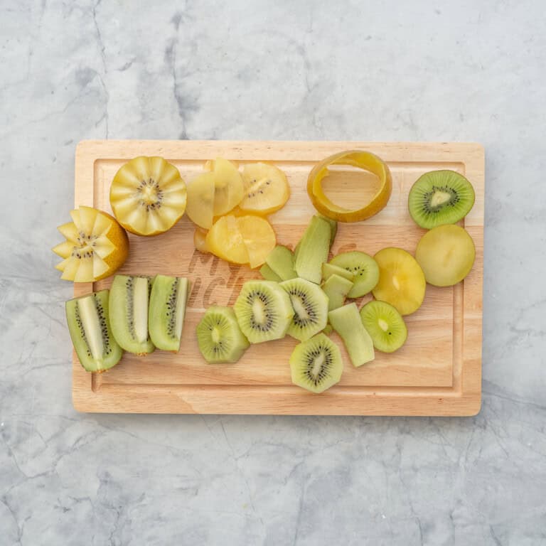 Different shaped pieces of green and gold kiwi cut on a wooden chopping board.