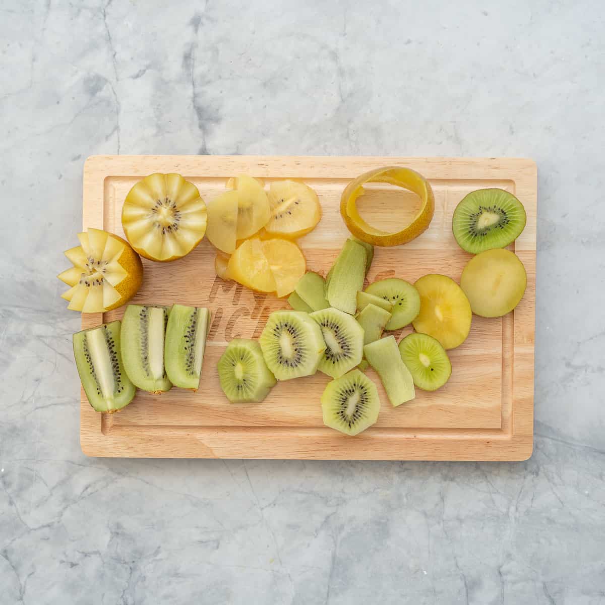 Different shaped pieces of green and gold kiwi on a wooden chopping board. 