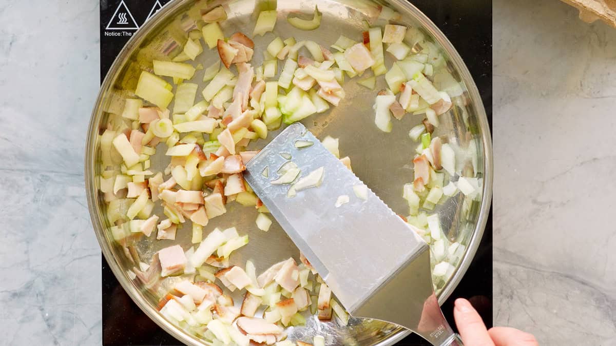 Diced onions and bacon cooking in oil in a stainless steel skillet.