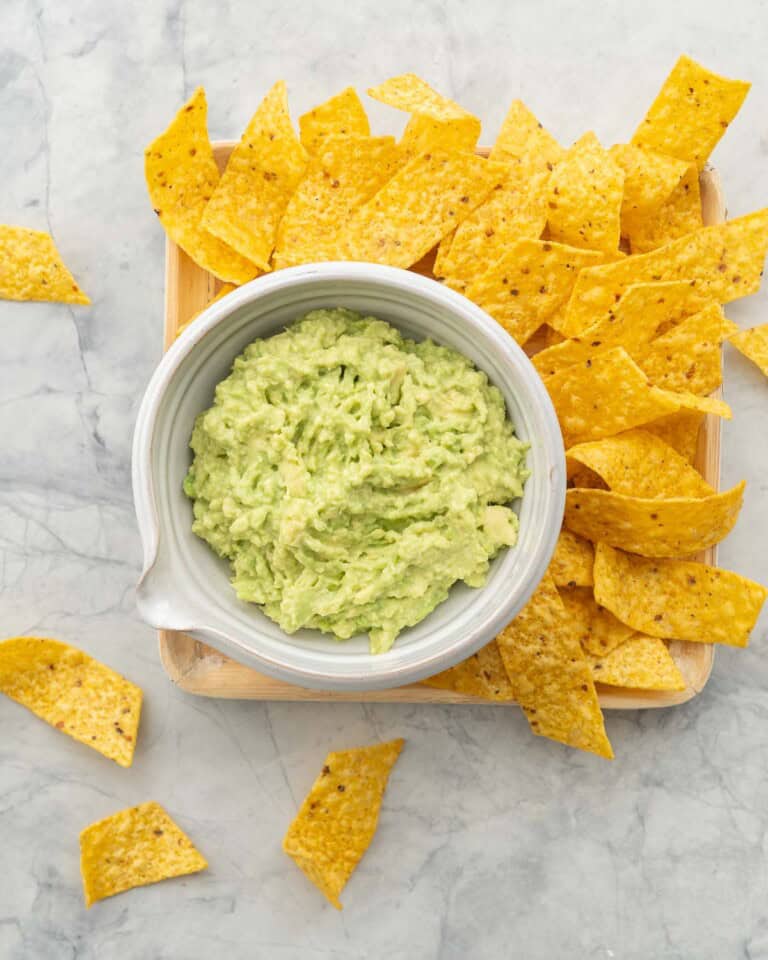 Guacamole in a bowl on wooden board surrounded by nacho chips.