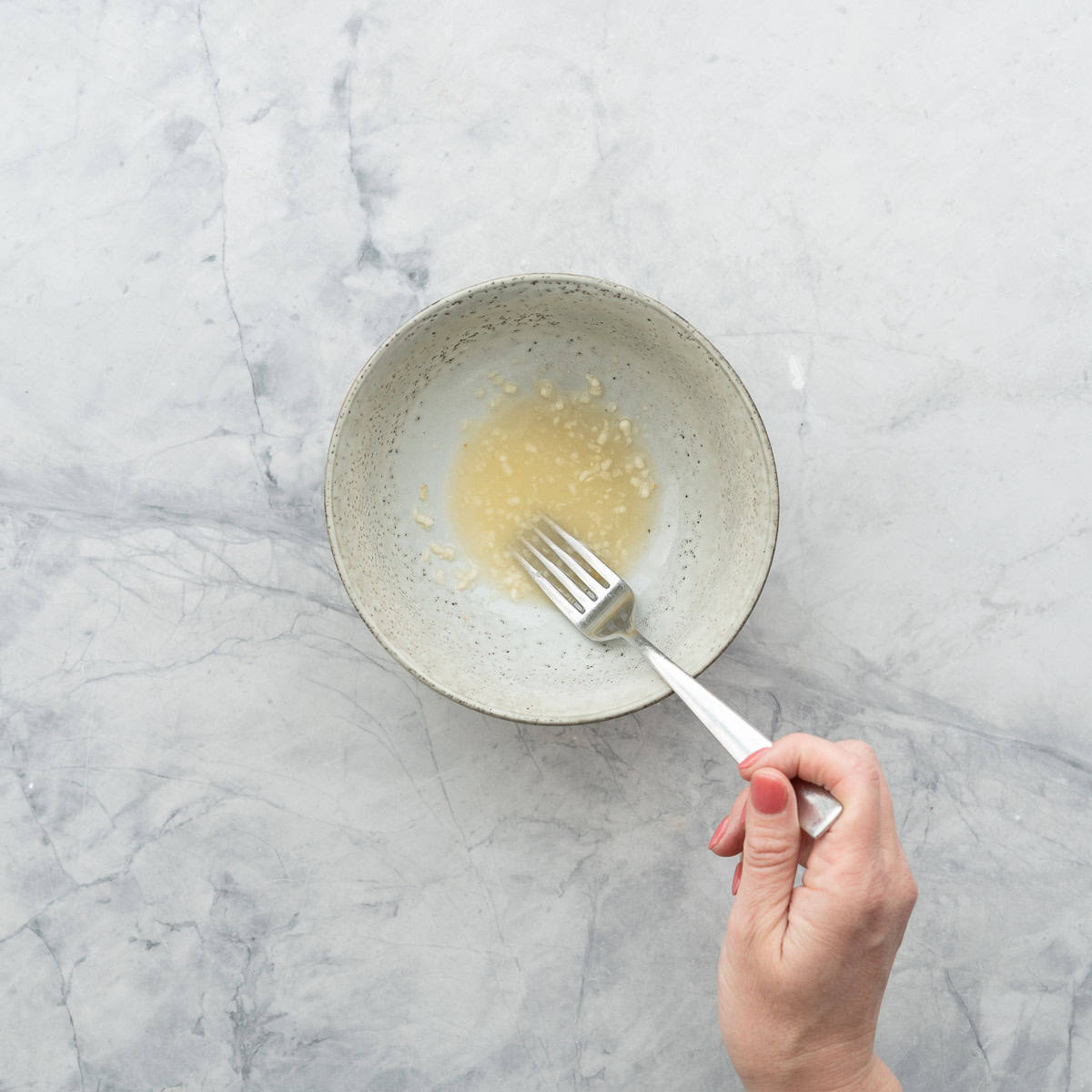 Fork mixing together crushed garlic, lemon juice and salt in a bowl.