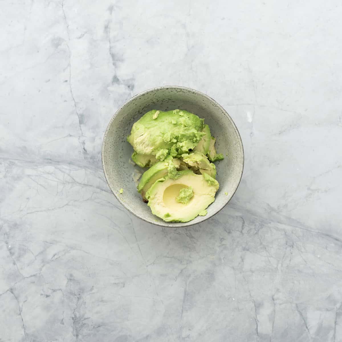 Avocado flesh added into bowl with garlic, lemon juice and salt.