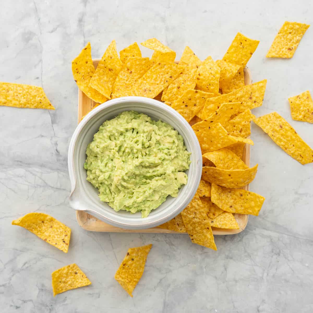 Guacamole in a bowl on wooden board surrounded by nacho chips.