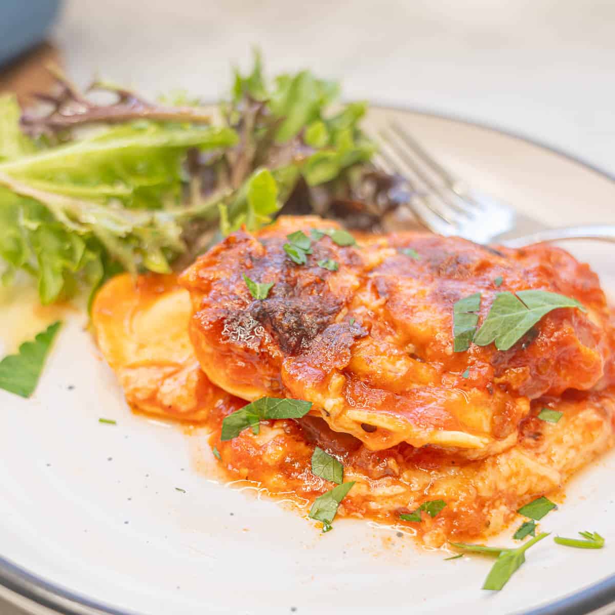 Plate of lasagna served with side salad and fork.