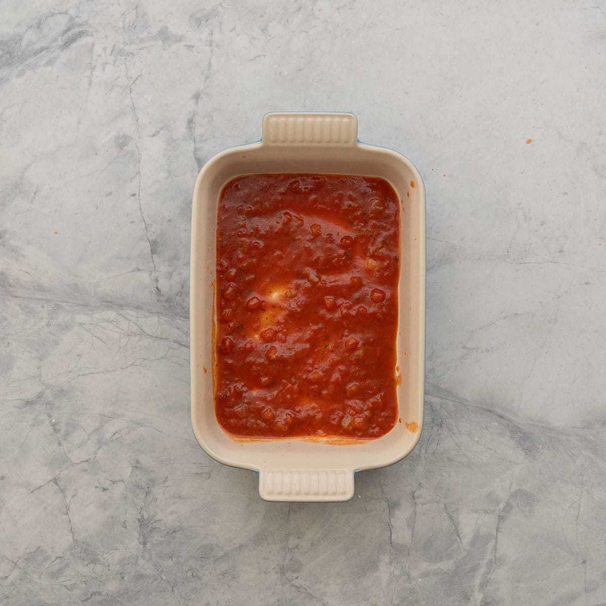 Pasta sauce lining the bottom of the baking dish.