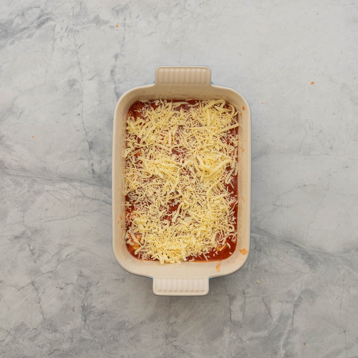 Lazy lasanga being layered in baking dish, pasta sauce, ravioli and cheese sprinkled on top.