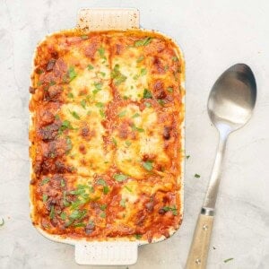 Lazy Lasagna in baking dish with serving spoon on bench top.