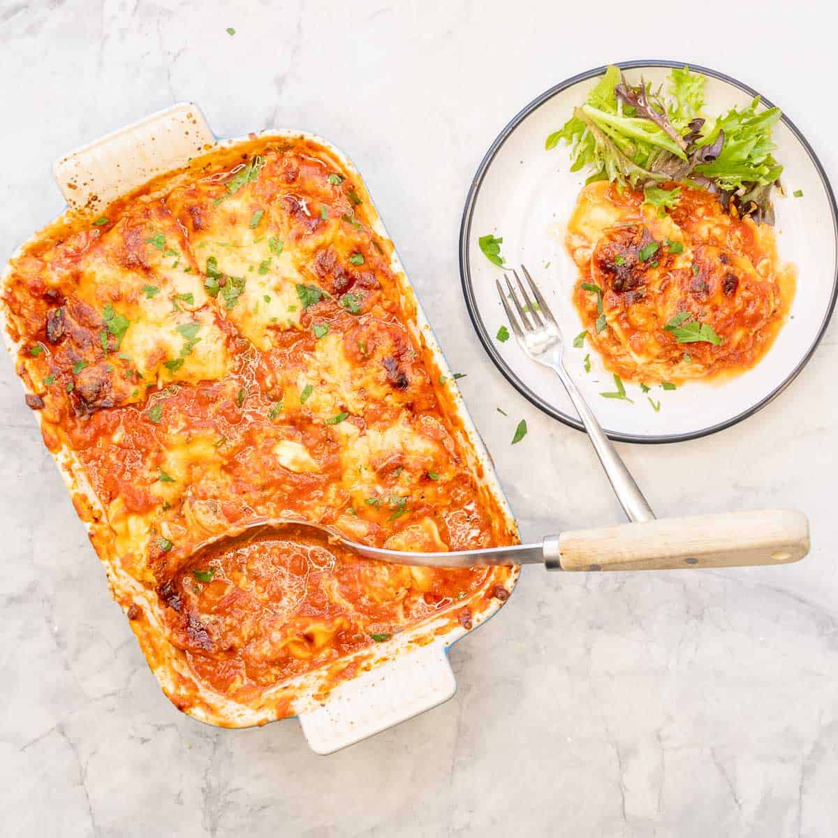 Lazy lasagna cooked in baking dish with serving spoon, portion served on a plate with a side salad and fork.