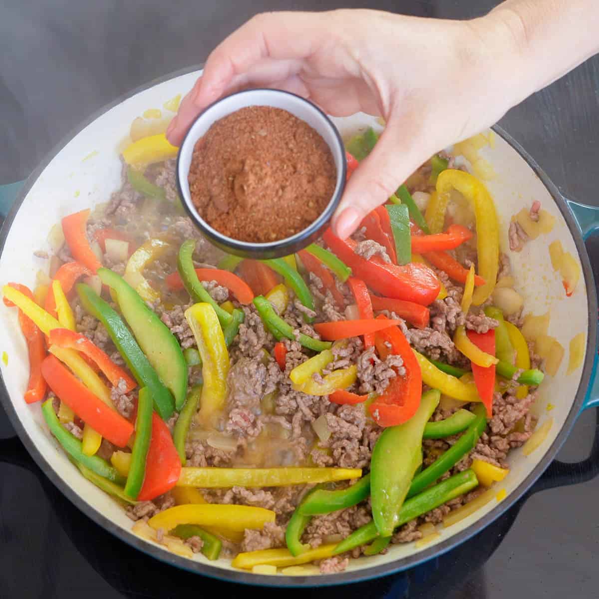 Mexican seasoning being added to capsicum and mince on stove.