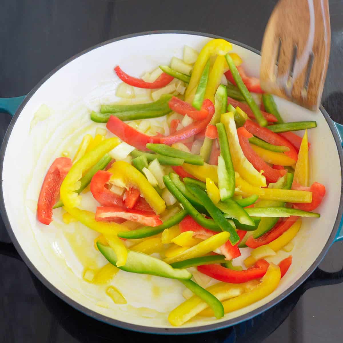 Green, yellow and red capsicum being stirfried in pan.