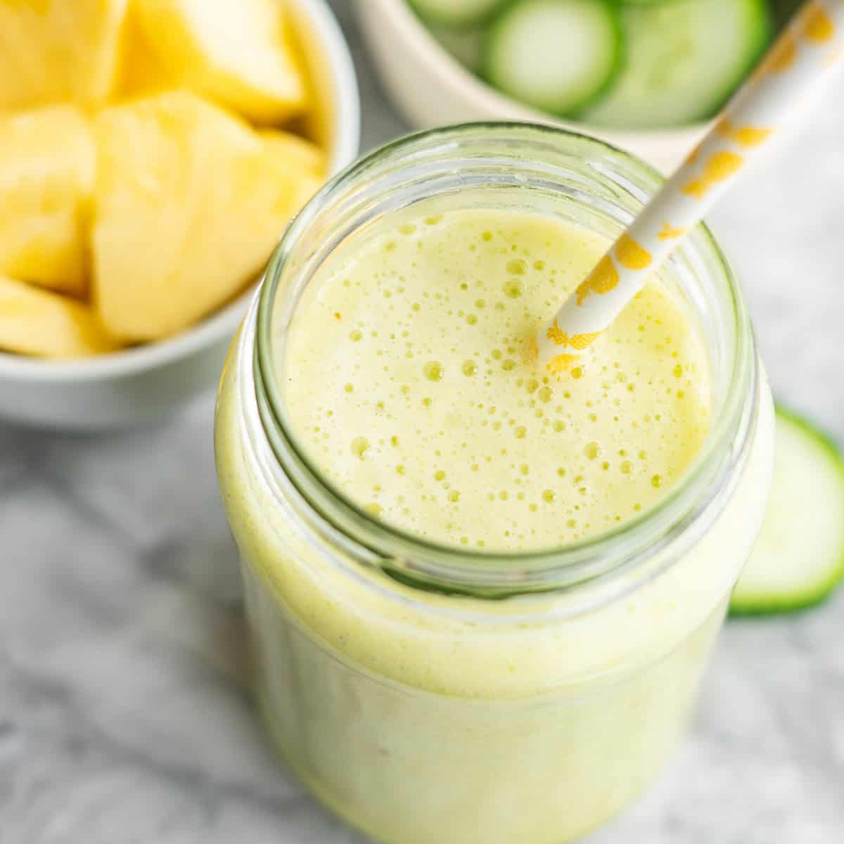 Looking down into a pineapple cucumber smoothie in glass with straw.