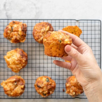 Pizza muffin held up by hand with cooling rack in background.