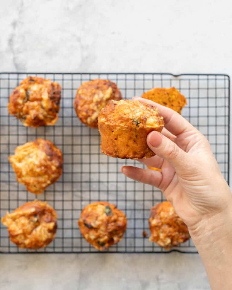 Pizza muffin held up by hand with cooling rack in background.