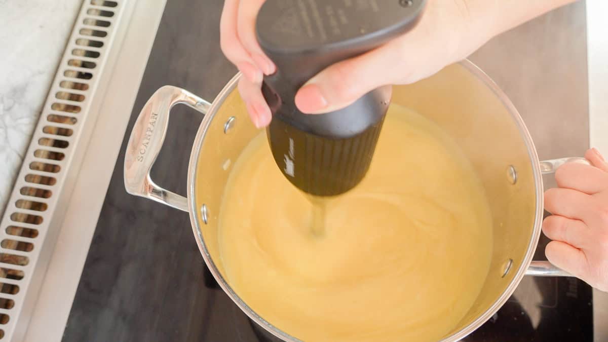 Electric hand food blender inside the pot on stove blending up the potatoes to make a smooth consistency.