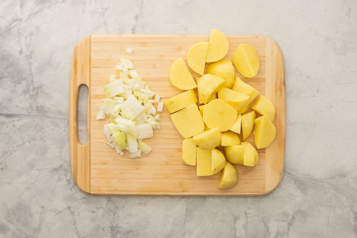 Chopped onion and potatoes on chopping board.