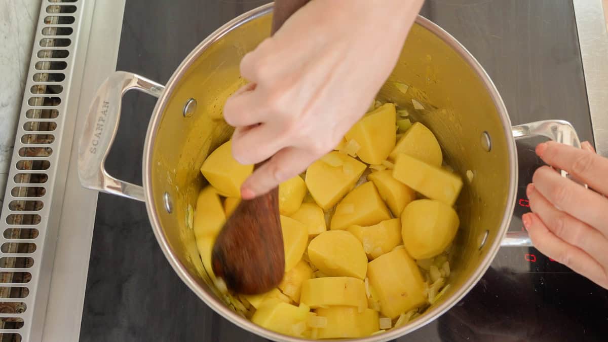 Potato and onion being mixed in pot on stove.