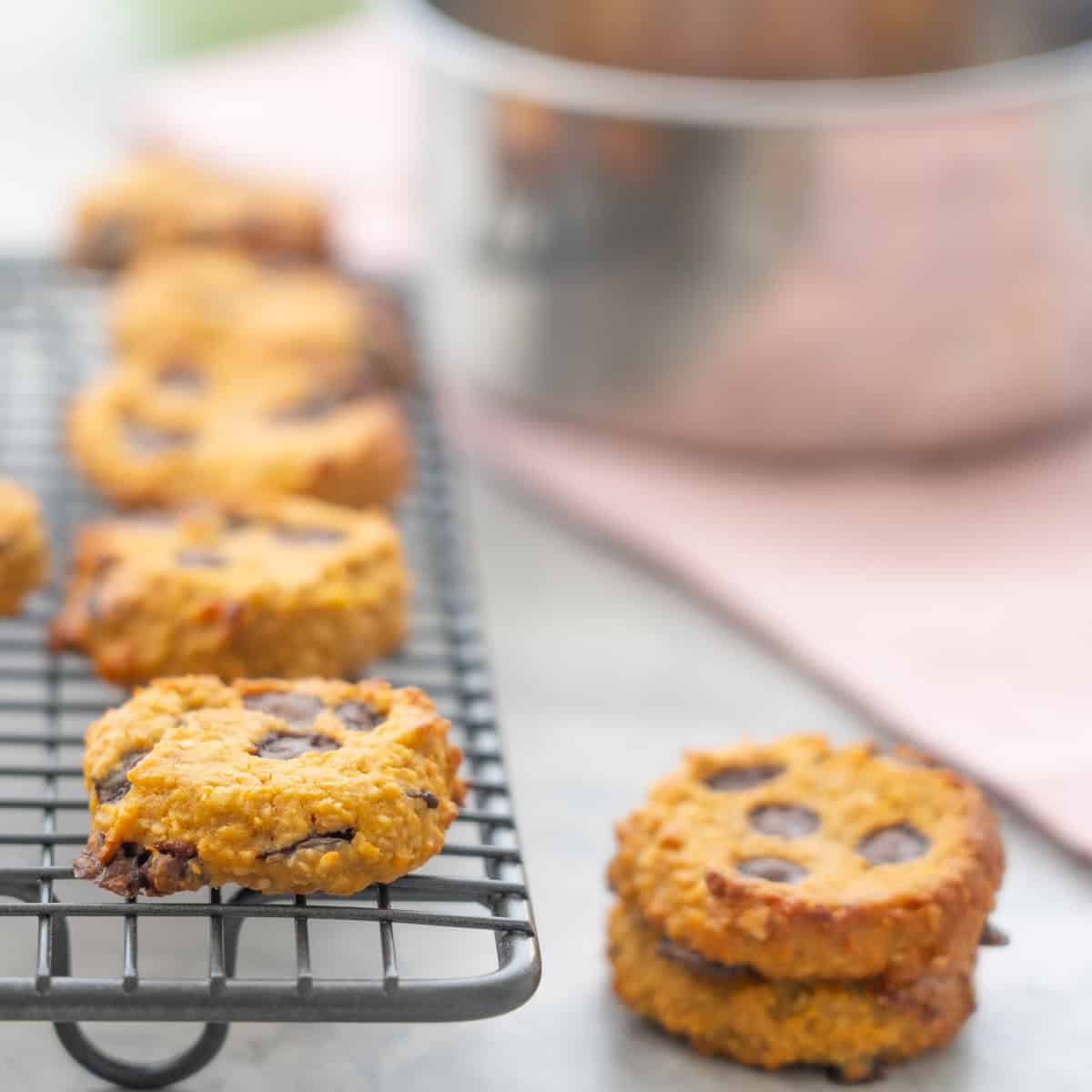 Two cookies stacked on each other next to a cooling rack with more Pumpkin cookies on top.