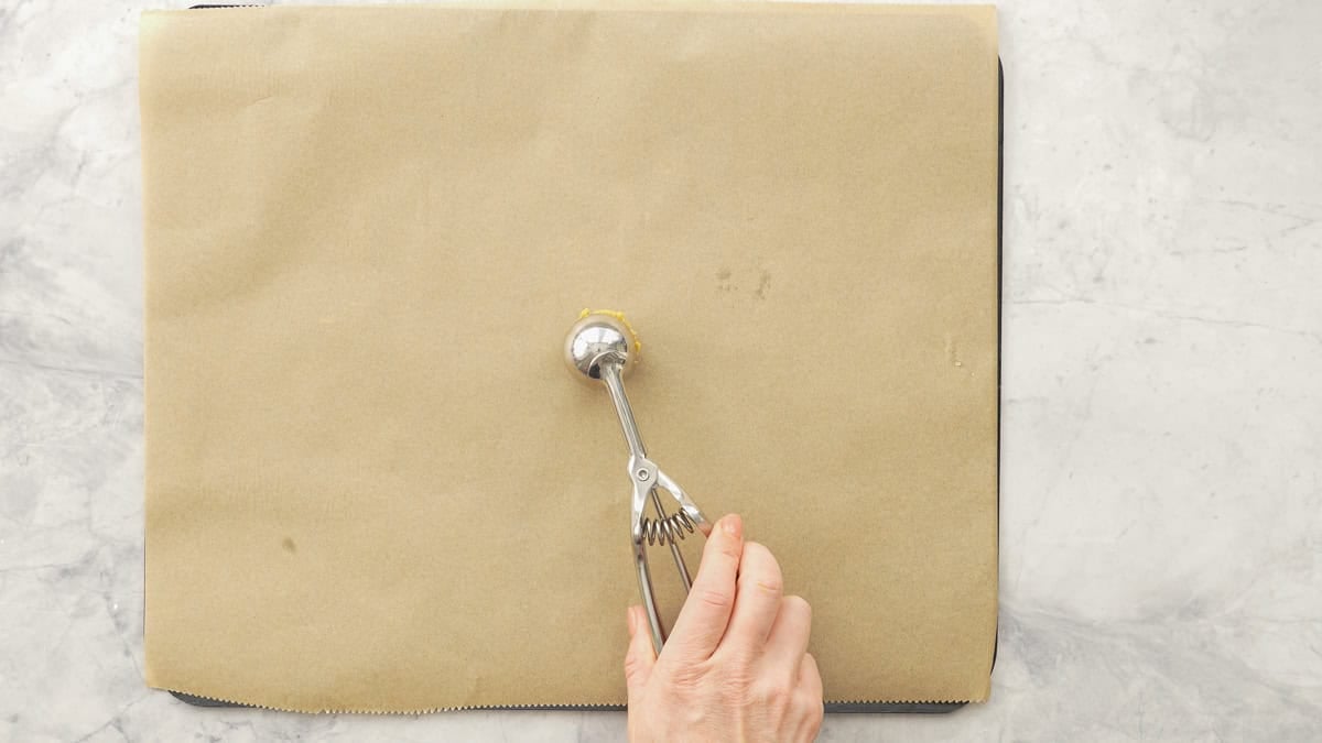 A hand using a little ice cream scoop to place Pumpkin cookie mixture onto tray lined with baking paper.