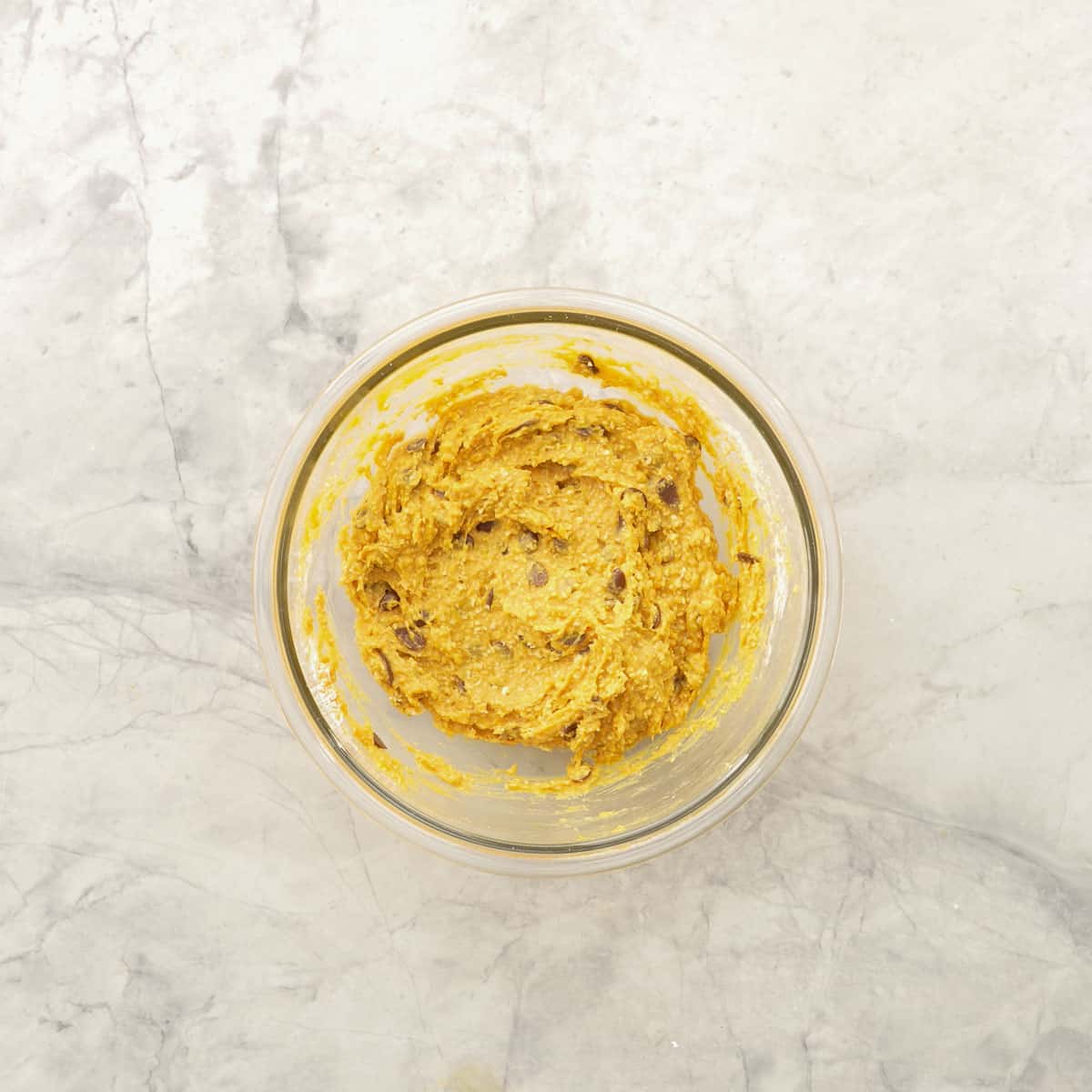 Ingredients for pumpkin cookies mixed together in glass bowl on bench top.