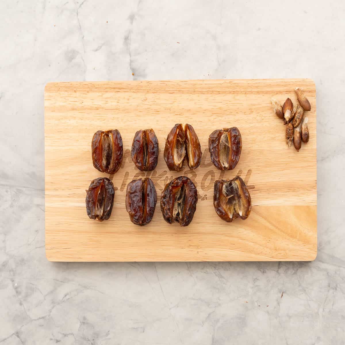 Dates on wooden chopping board cut lengthwise with stones removed.