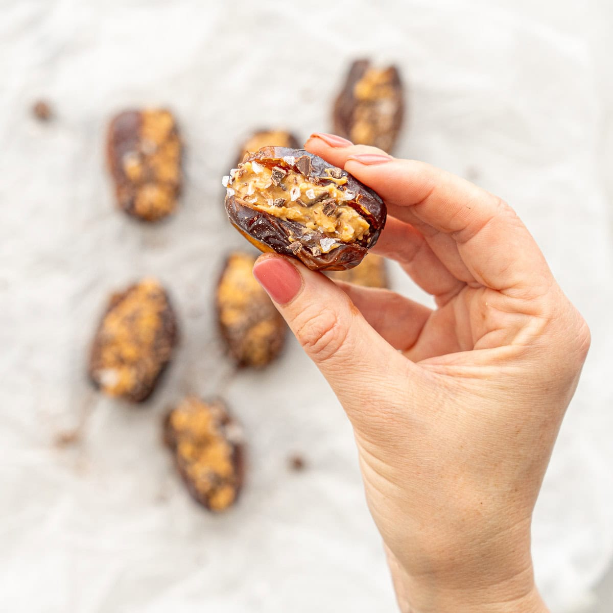 Hand holding a stuffed date up showing the peanut butter mixture inside with sprinkled salt on the top.