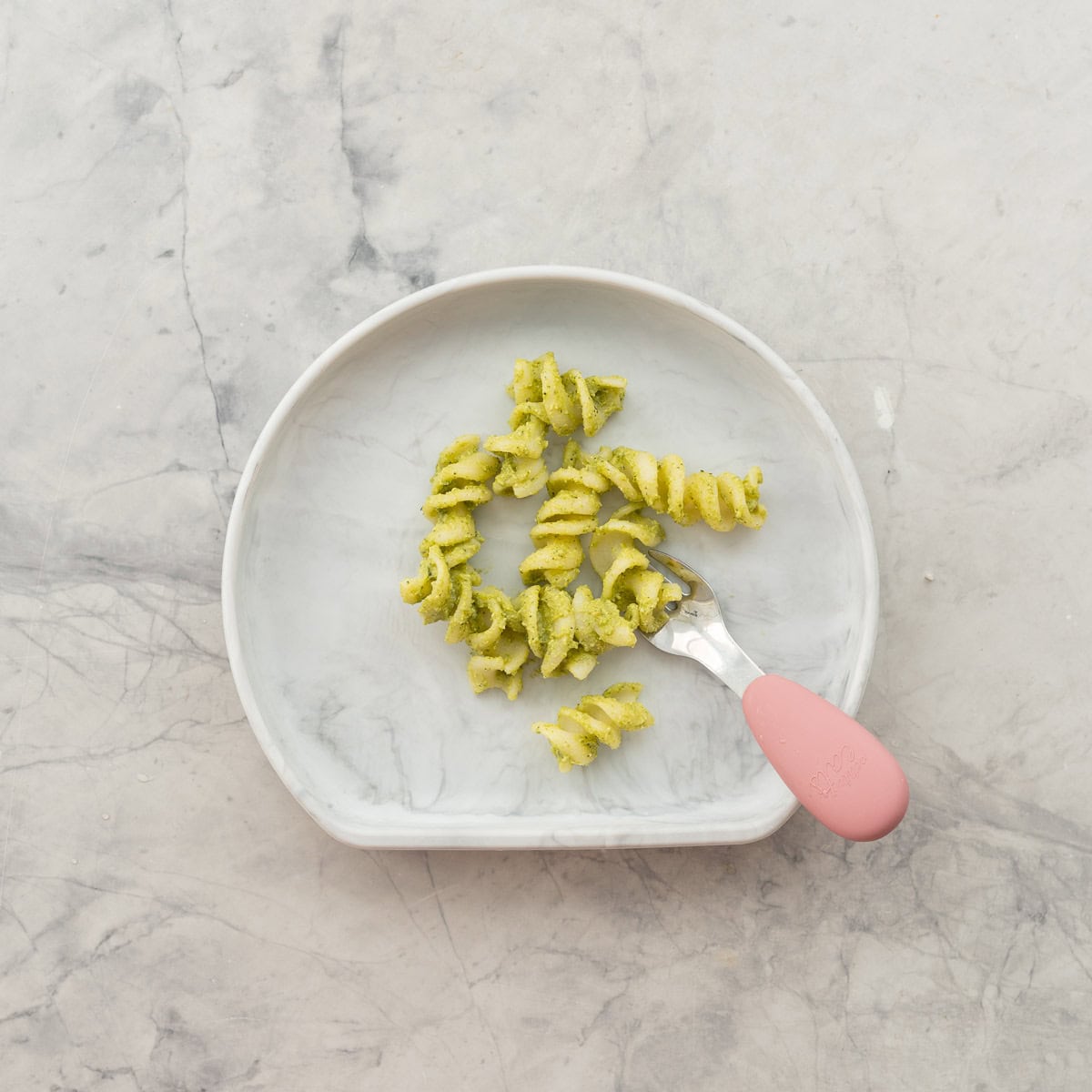 Spiralled pasta with avocado pasta mixture stirred through served on a silicone childs plate with childs fork.