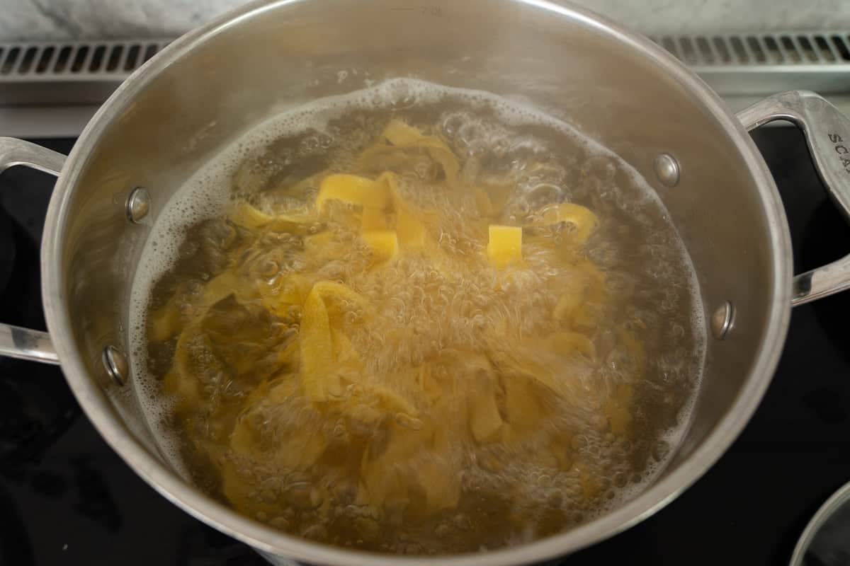 Pasta in boiling water in a pot on stove.