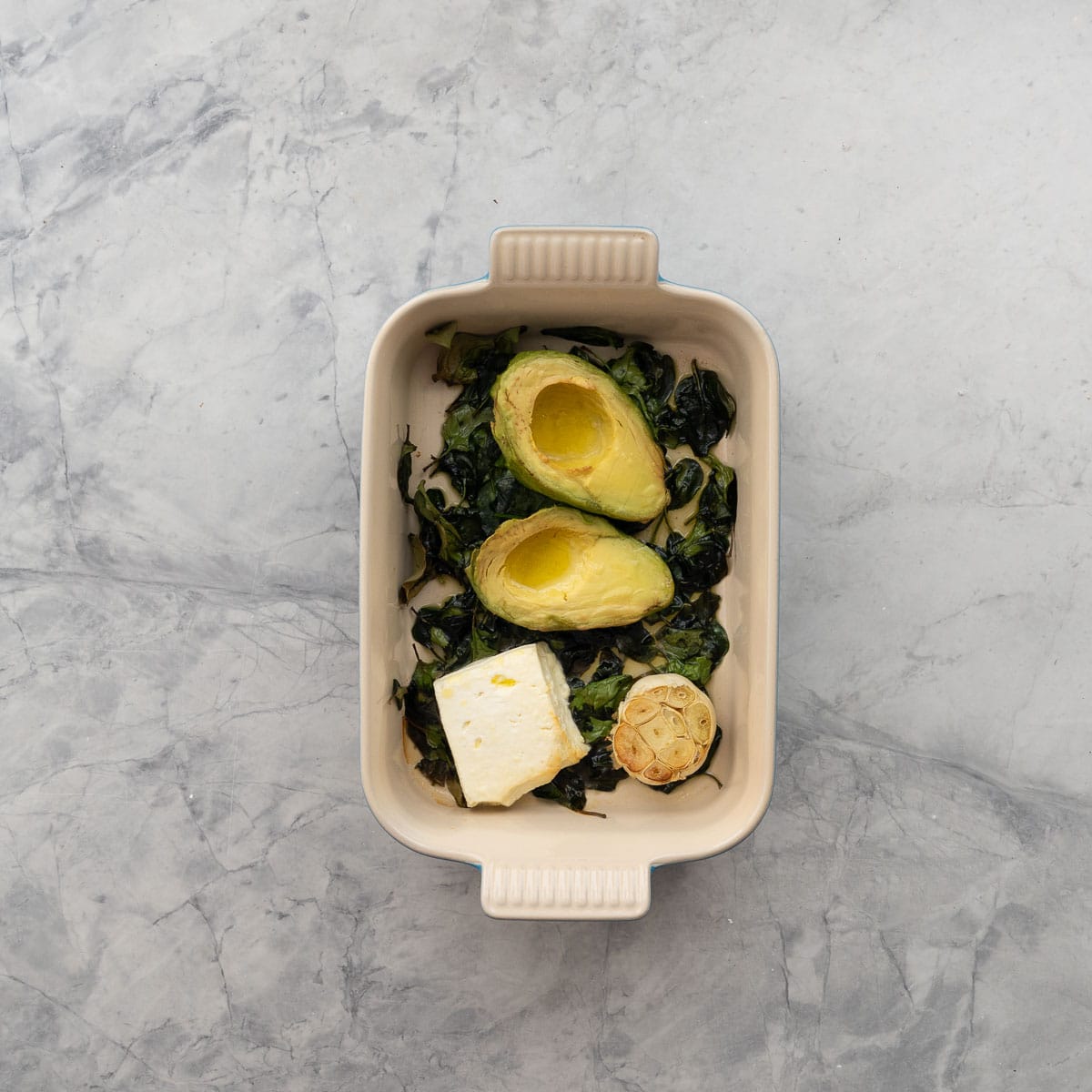 Spinach, avocado, feta cheese and garlic roasted in baking dish.