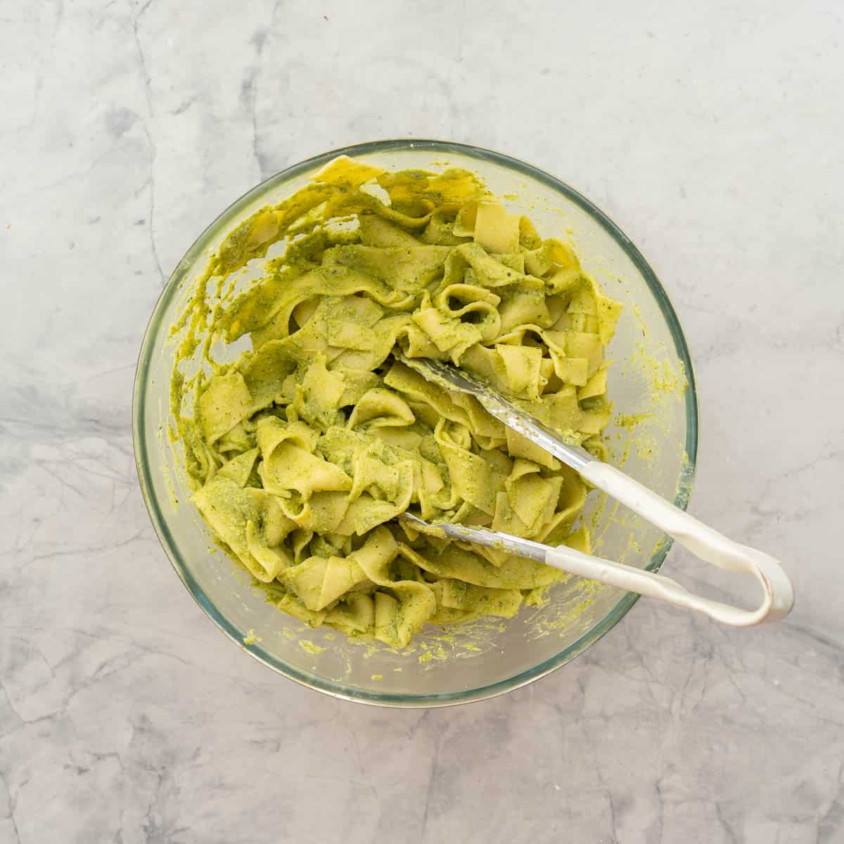 Blended avocado mixture mixed through cooked pasta with tongs.