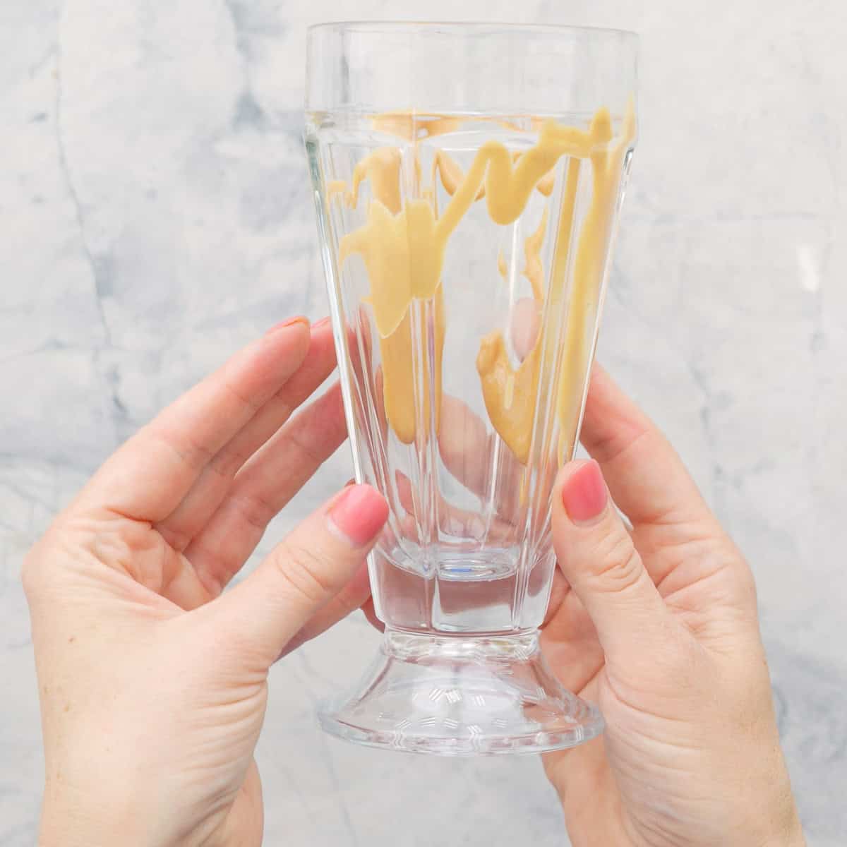 Peanut butter drizzled around the inside of a glass smoothie cup being held by hands.