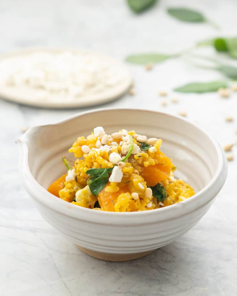 Served up portion of Crockpot pumpkin risotto garnished with pine nuts and crumbled feta cheese in a bowl on benchtop.