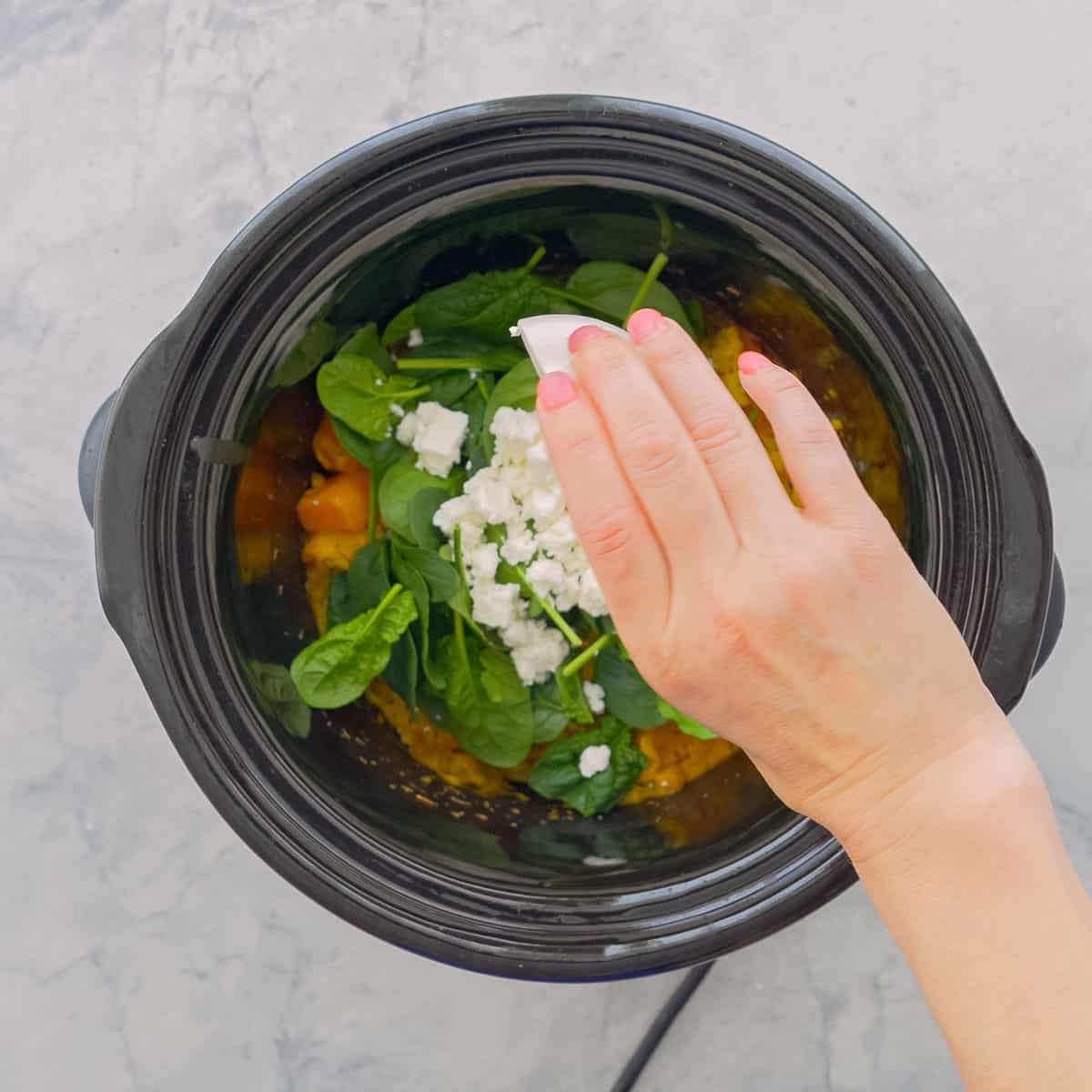 Fresh spinach and feta cheese being poured on top of the crockpot risotto pumpkin.