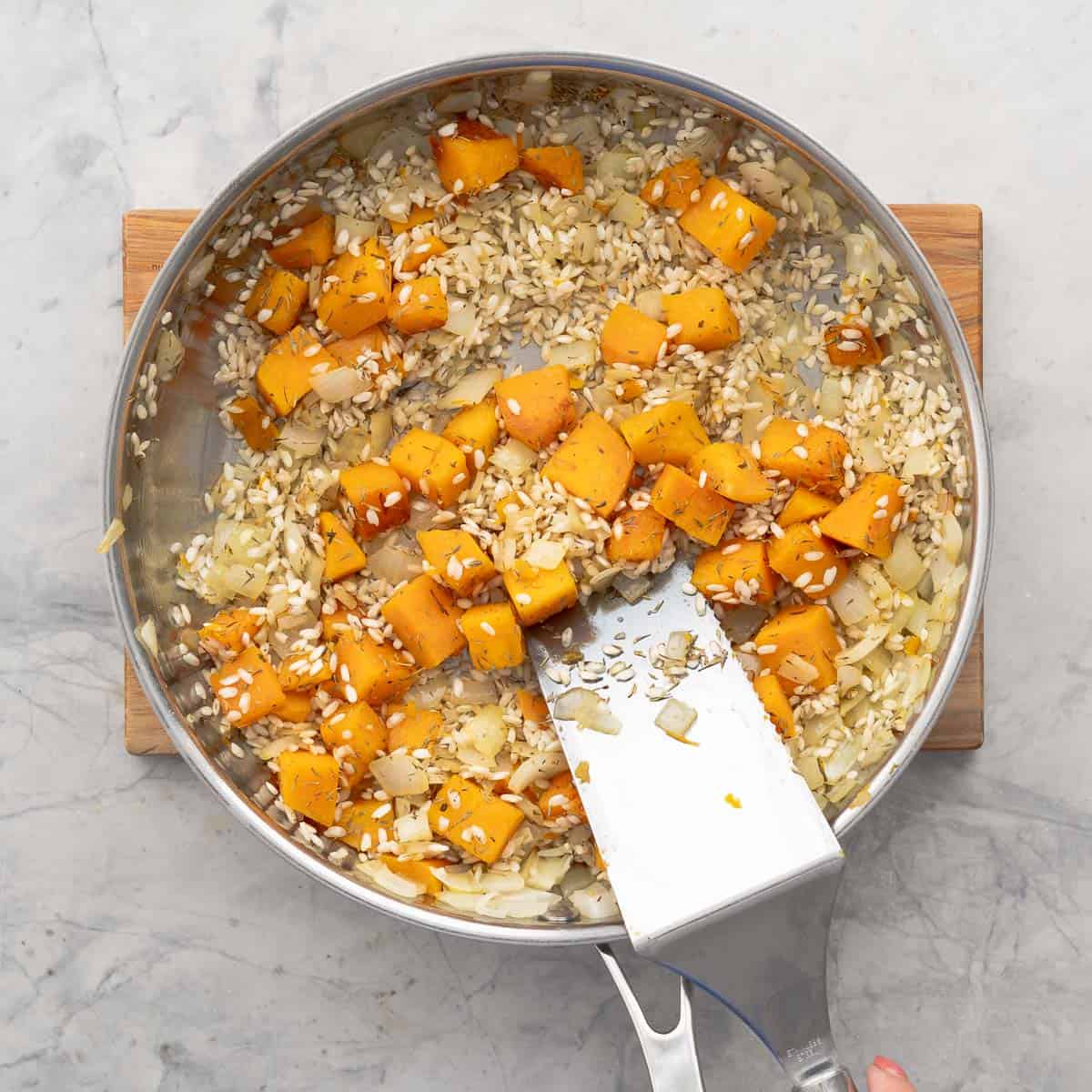 Rice, pumpkin, onion and thyme sautéed. Fry pan on wooden chopping board on benchbenchtoptop.