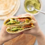 Falafel pita cut in half being held by a persons hands showing the layers of ingredients inside.
