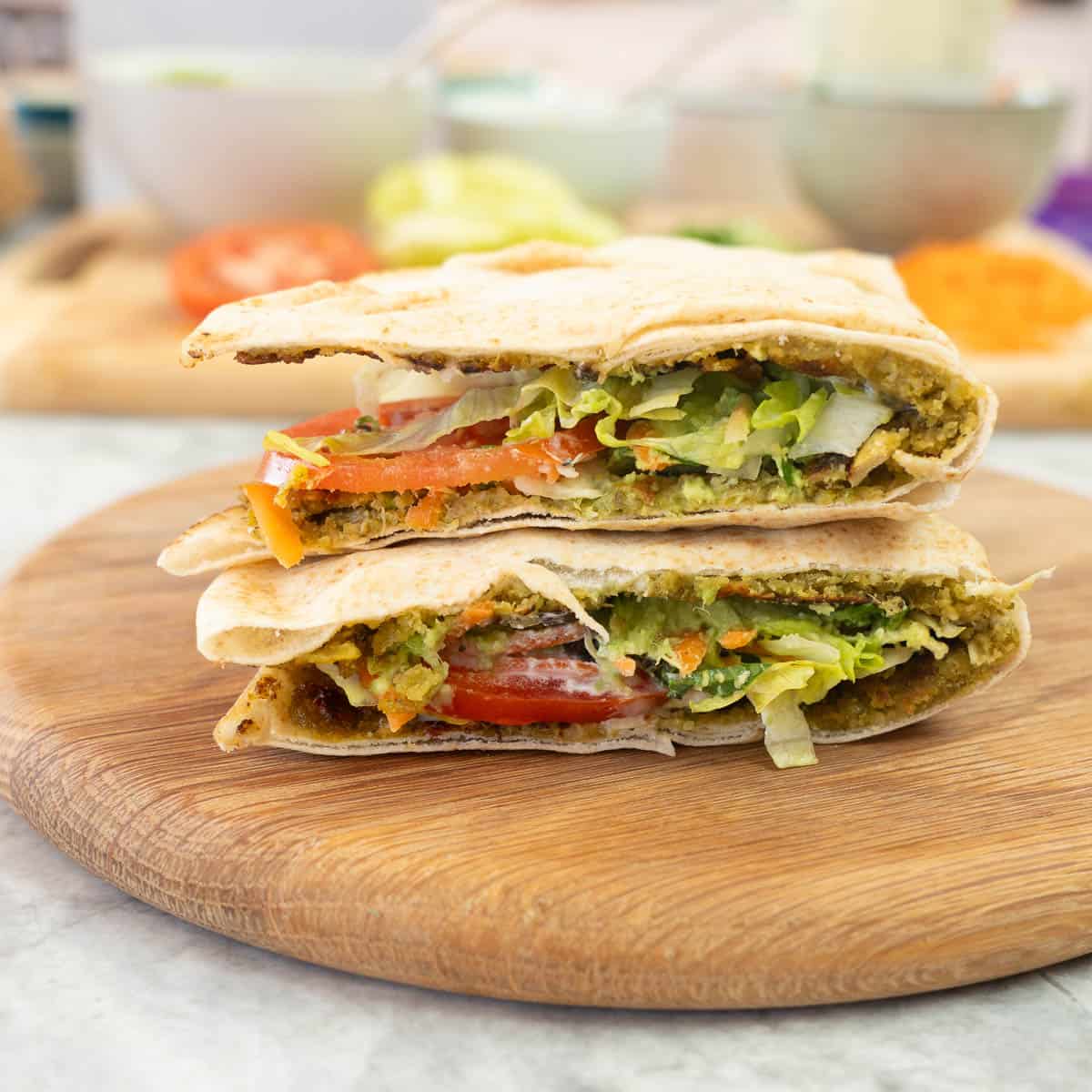 Falafel pita cut in half on wooden chopping board showing the layers of ingredients inside.