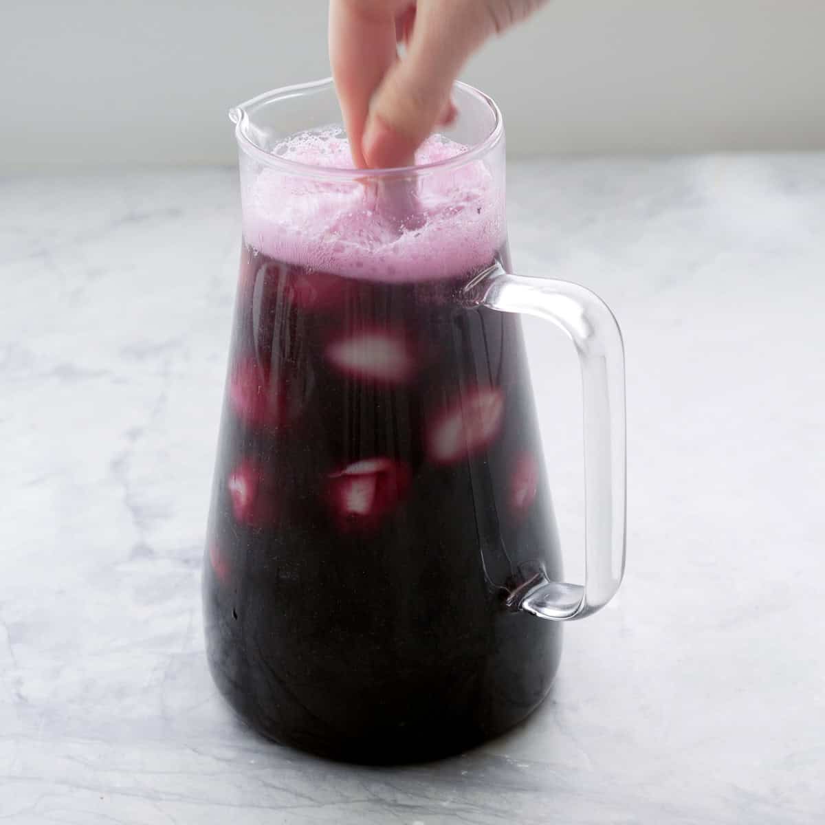 Hand holding ladle string halloween punch in glass jug.