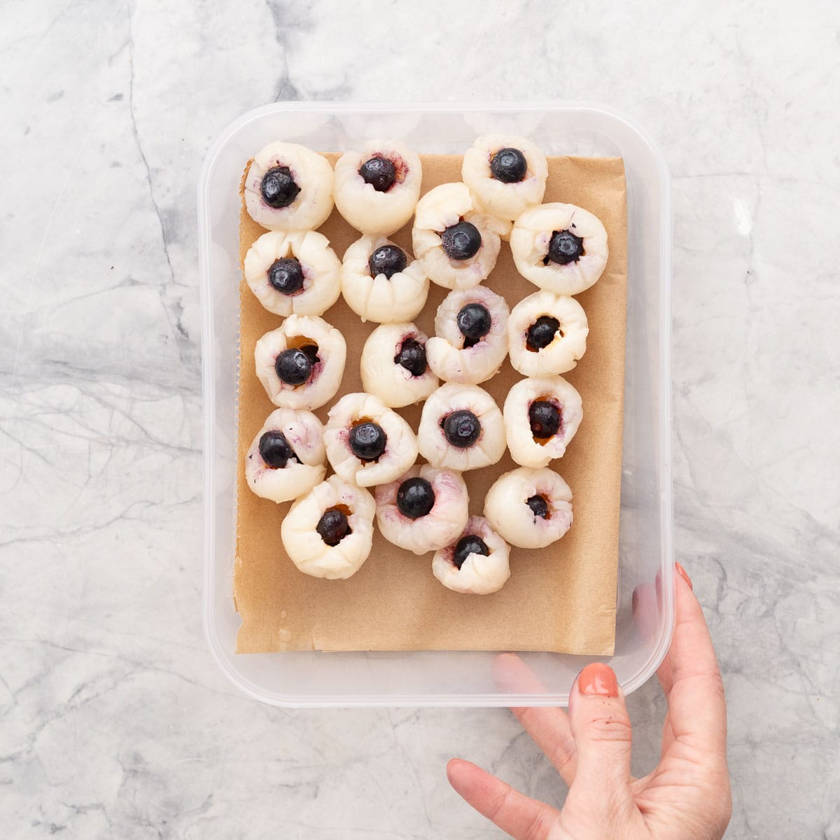 Lychees stuffed with frozen blueberries in a lined container.