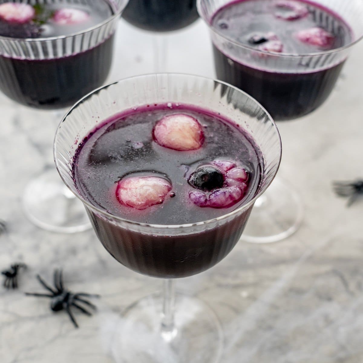 Halloween punch in tall glass, lychee and blueberry looking eyeballs floating on the top of the punch. Fake spiders and cobweb on benchtop.