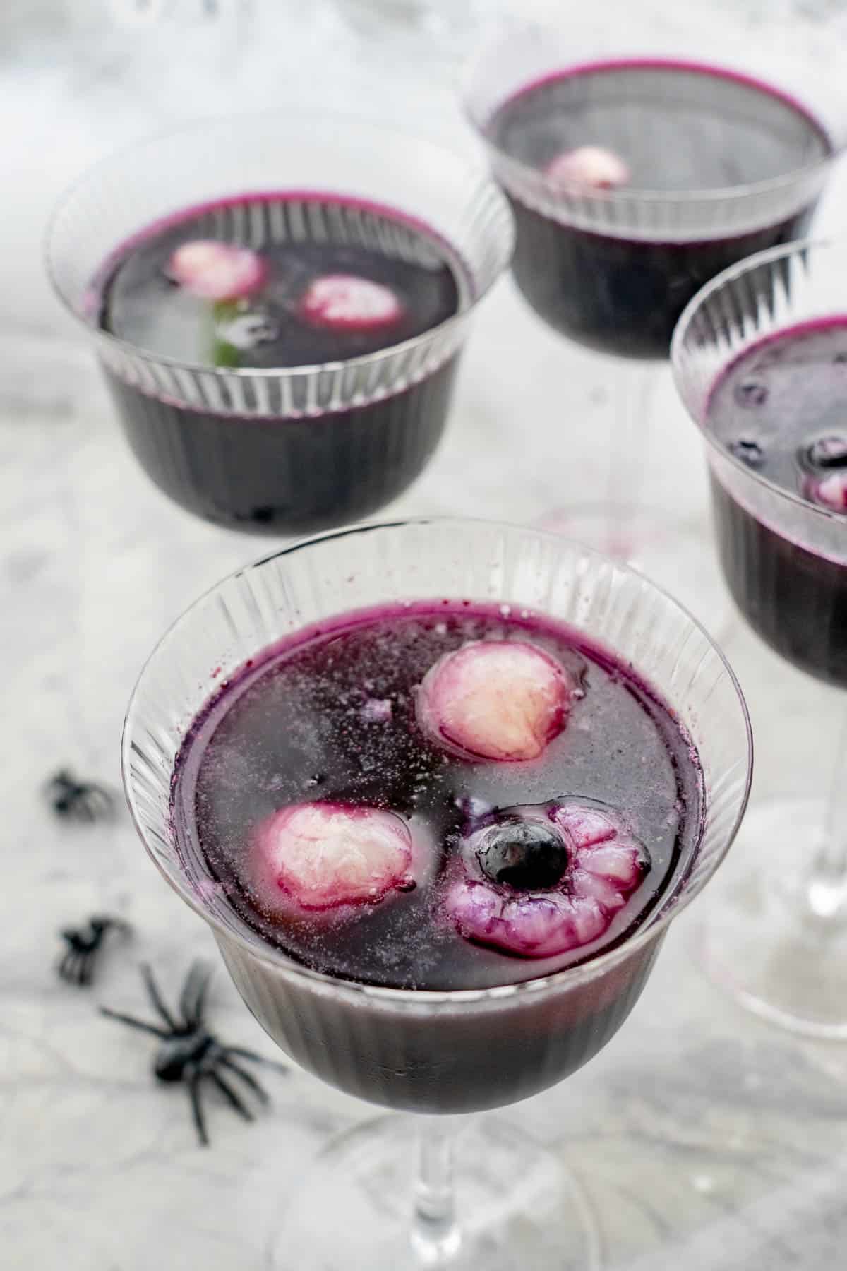 Halloween punch in tall glass, lychee and blueberry looking eyeballs floating on the top of the punch. Fake spiders and cobweb on benchtop.