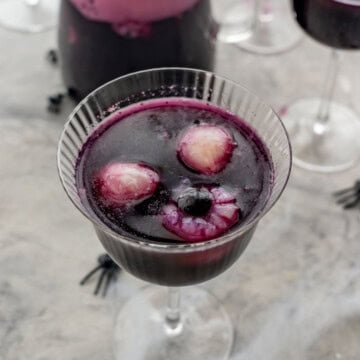 Halloween punch in tall glass, lychee and blueberry looking eyeballs floating on the top of the punch. Fake spiders and cobweb on benchtop.