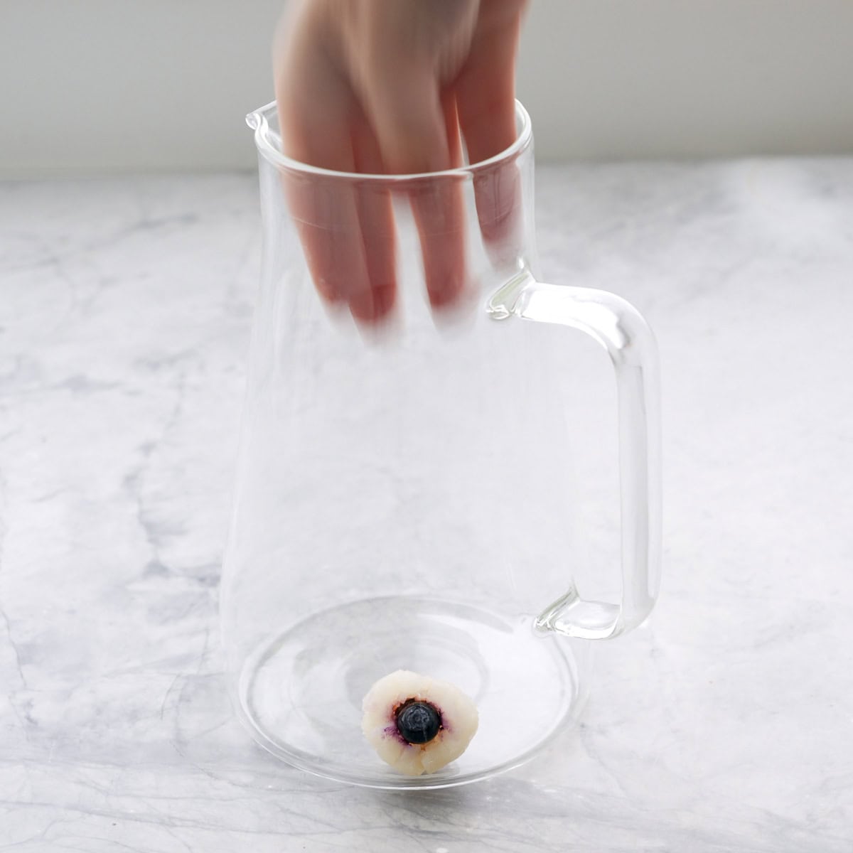 Lychee and blueberry eyeball being placed onto the bottom of the glass jug.